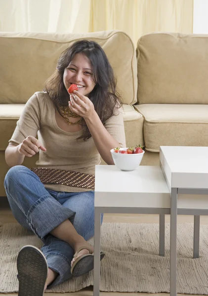 Young woman eating strawberries on living room floor