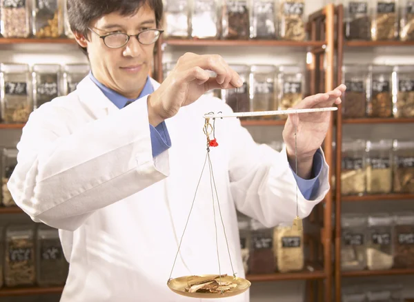 Asian male herbalist doctor weighing Chinese medicinal herbs