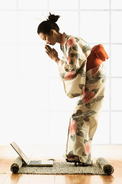 Side profile of a young woman wearing a kimono standing in front of a laptop