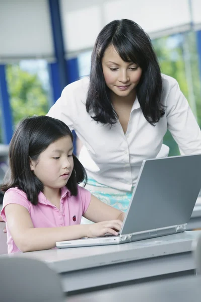 Teacher helping girl on laptop