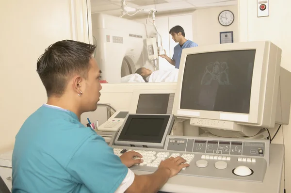 Male nurse using computer as young woman gets a CT scan