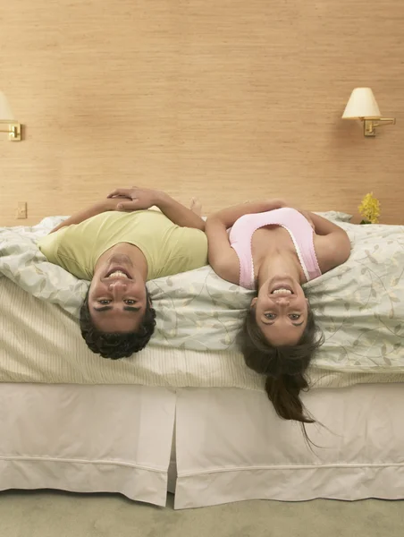 Couple hanging heads over the edge of bed