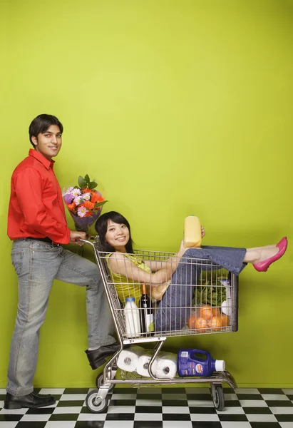 Man pushing woman in shopping cart with groceries