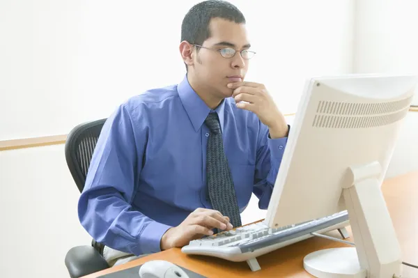 Businessman at desk with hand on chin in front of computer