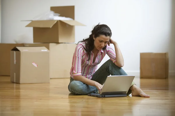 Young adult woman sitting on floor with computer with moving boxes