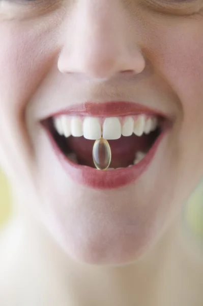Young woman holding a pill between her teeth