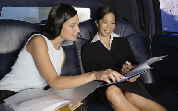 Two businesswoman reading paperwork in backseat of car