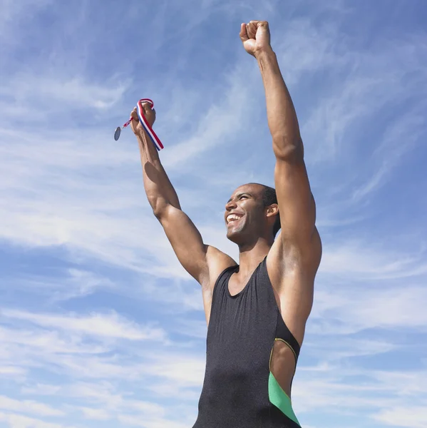 African male athlete cheering while holding medal