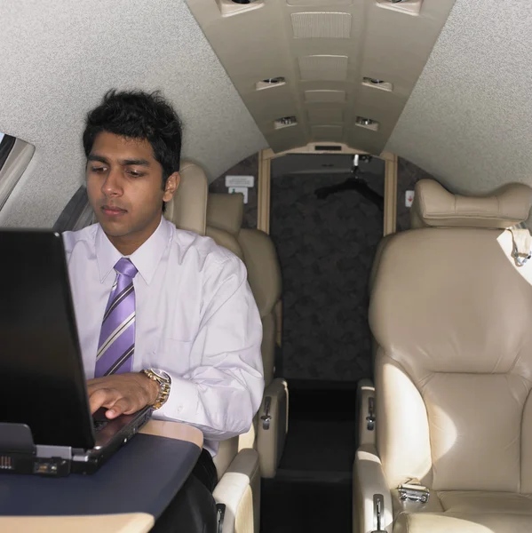 Young Indian businessman working on laptop inside airplane