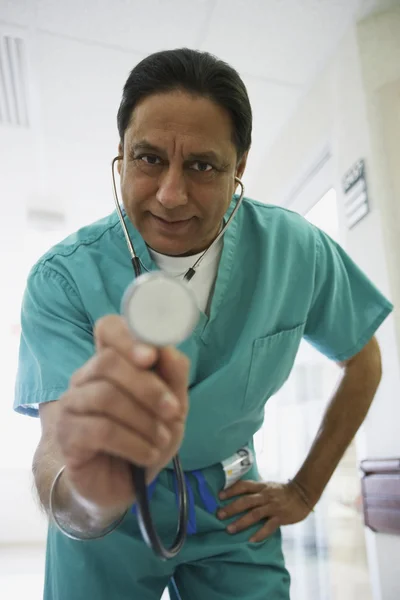 Middle-aged Indian male doctor holding out stethoscope