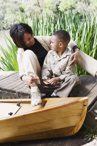 African mother and son sitting on dock next to canoe