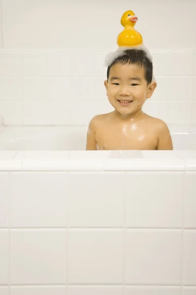 Young Asian boy with rubber duck on head in bubble bath