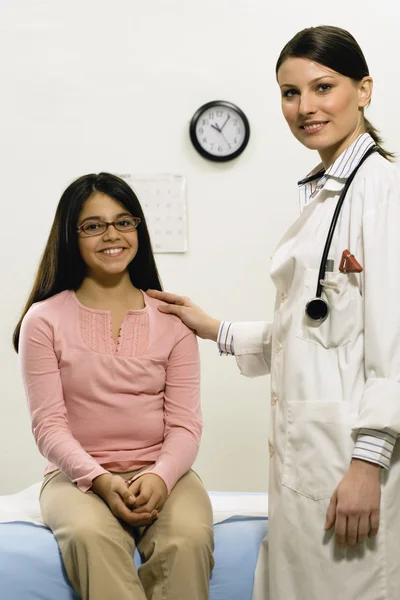 Female doctor with hand on young female patient\'s shoulder
