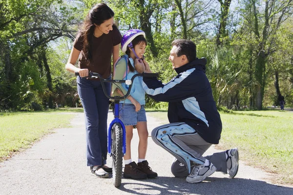 Hispanic father helping daughter fasten bicycle helmet
