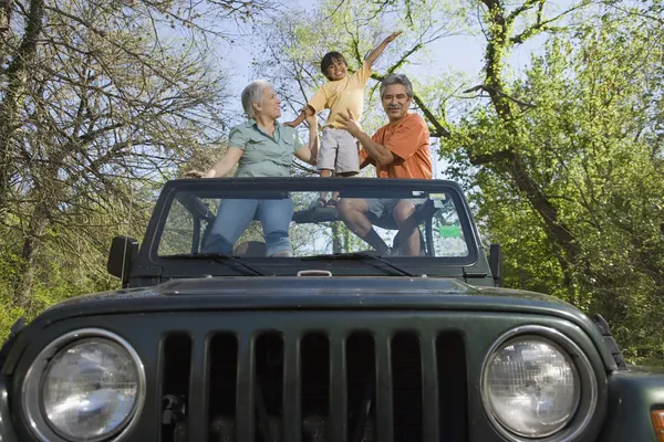 Grandparents and grandson standing in jeep