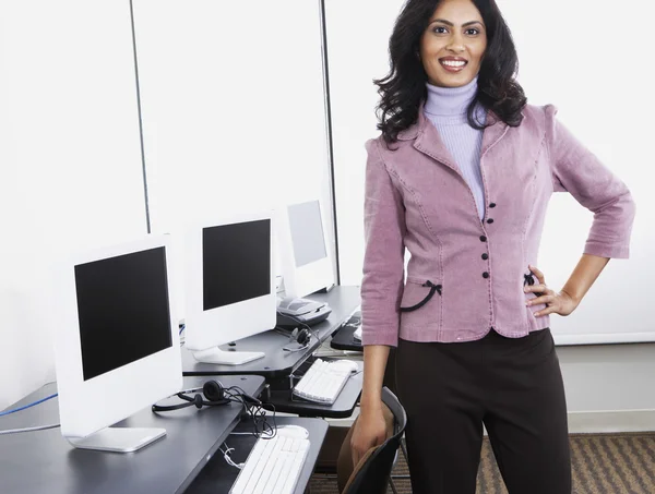Indian businesswoman standing next to computers smiling