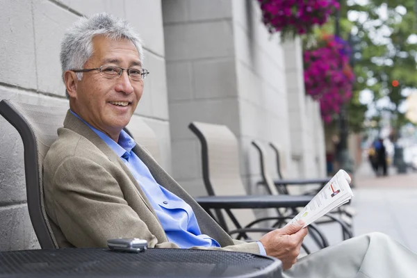 Senior Asian man reading at outdoor cafe
