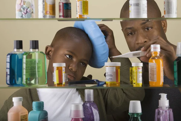 African father taking son\'s temperature in front of medicine cabinet