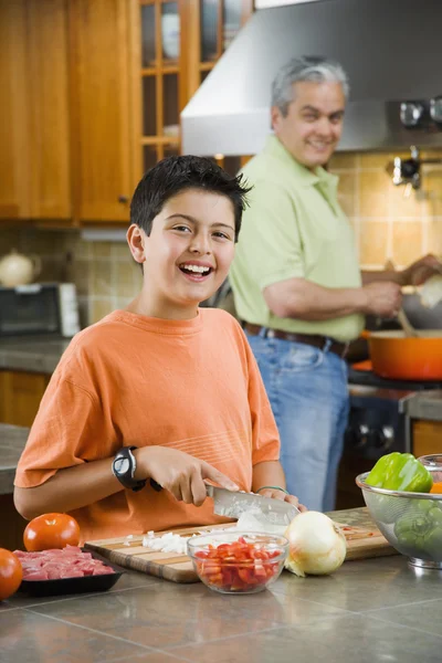 Hispanic father and son cooking and chopping vegetables in kitchen