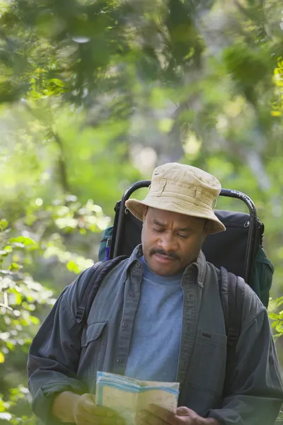 African man with map wearing backpack in woods