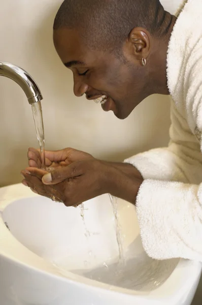 African man washing face in sink