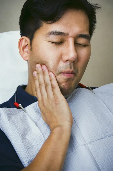 Asian male dental patient holding jaw