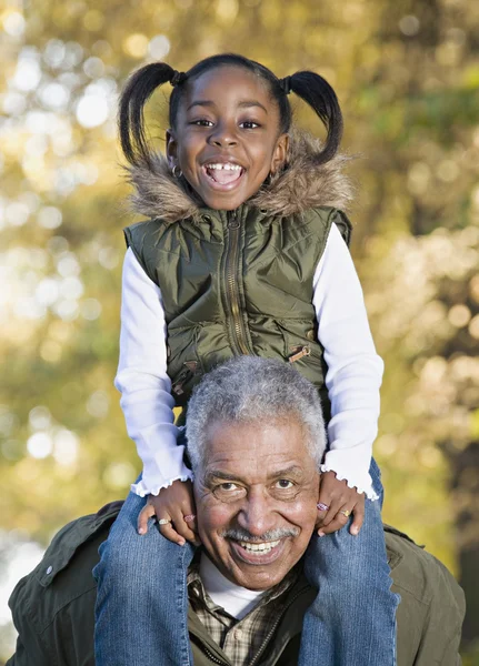 African grandfather carrying granddaughter on shoulders