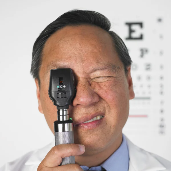 Asian male optometrist looking through medical instrument