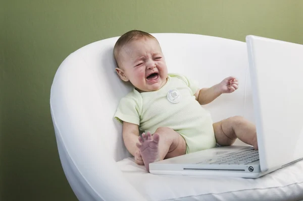 Crying baby in chair next to laptop