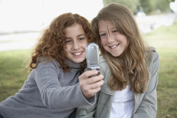 Two teenage girls using camera phone outdoors