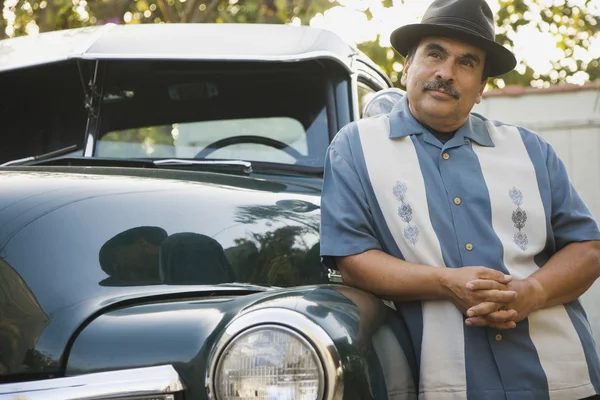 Middle-aged Hispanic man leaning against classic car