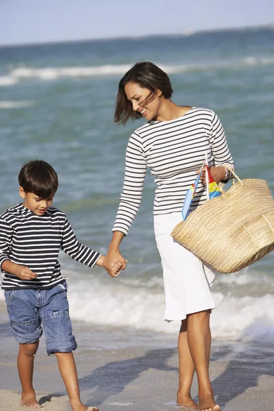 Indian mother and son holding hands and walking on beach