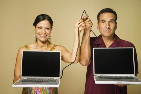Hispanic couple holding cable connecting two laptops
