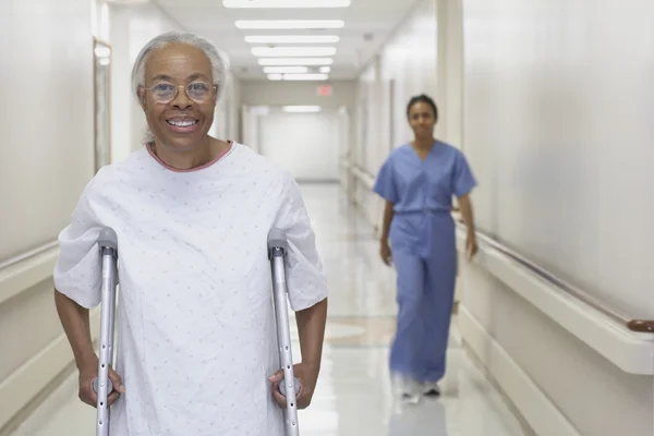 Senior African woman walking on crutches in hospital corridor