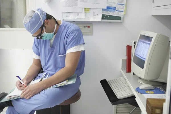Surgeon writing in chart next to computer