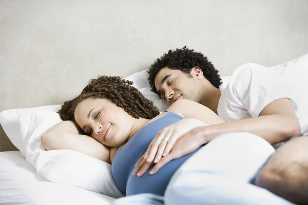 Pregnant African couple sleeping in bed