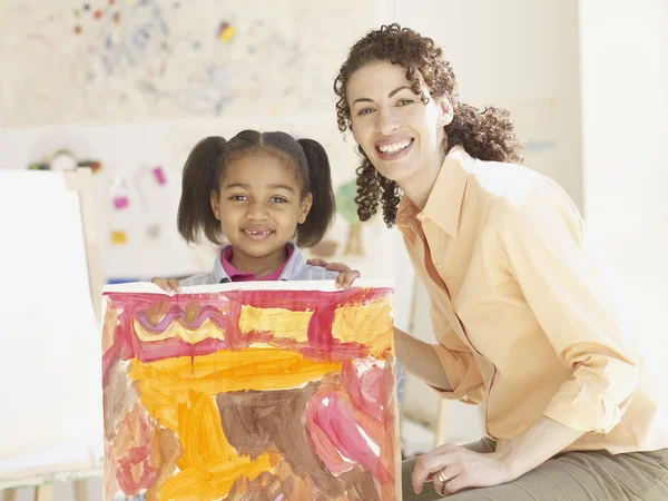 Hispanic female art teacher and female student holding painting