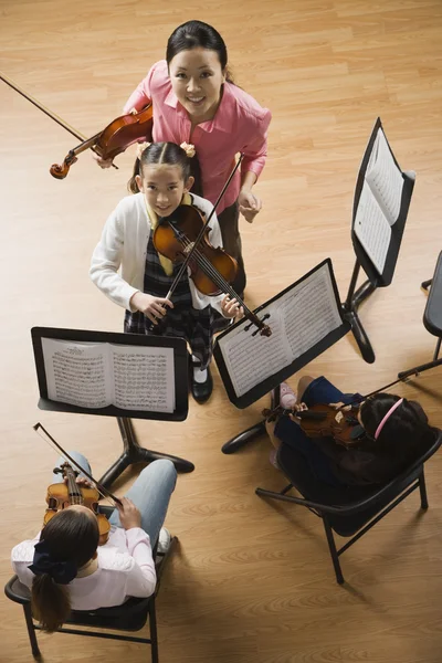 Asian female music teacher helping student play violin