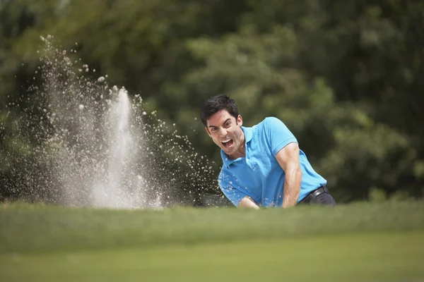 Hispanic man playing golf in sand trap