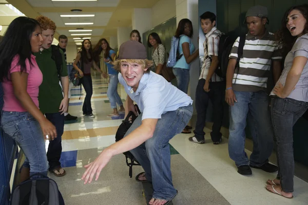 Teenaged boy riding skateboard in school hallway
