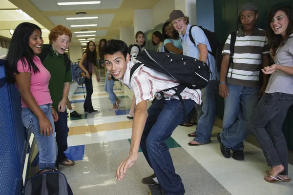 Hispanic teenaged boy riding skateboard in school hallway