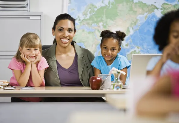 Mixed Race female teacher and students behind desk