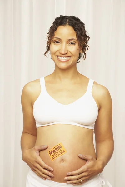 Pregnant Mixed Race woman with fragile sticker on belly