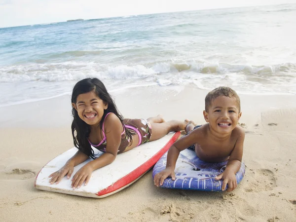 Pacific Islander siblings laying on boogie boards