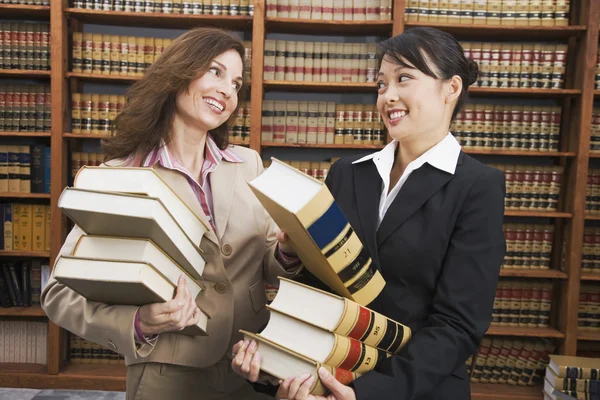 Multi-ethnic women carrying stacks of library reference books
