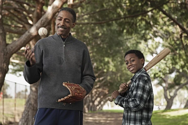 African man and son with baseball bat and glove in park