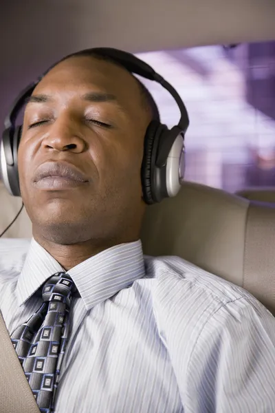 African businessman listening to headphones in back seat of car