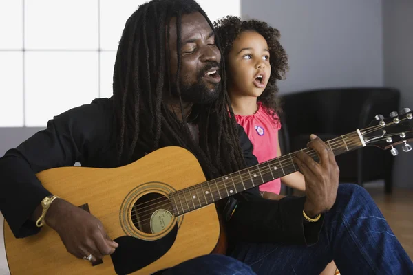 African father playing guitar, daughter singing