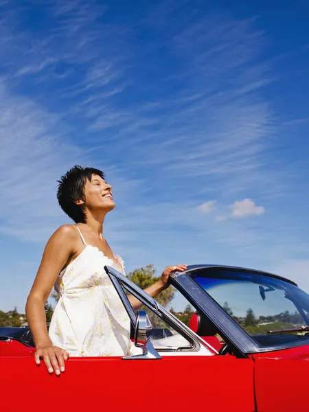 Mixed race woman standing near red convertible
