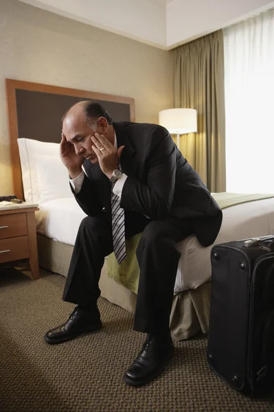 Middle-aged businessman sitting on bed in hotel room